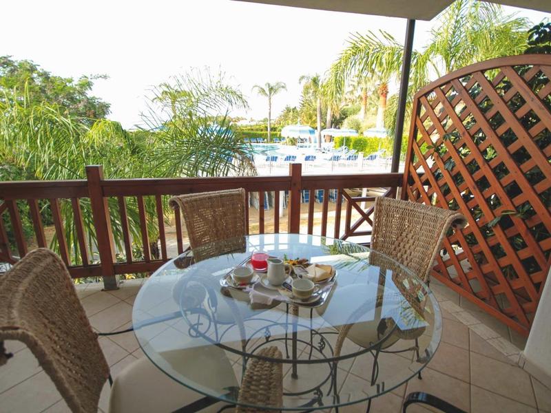 Balcon avec table en verre et quatre chaises donnant sur des palmiers et de l'eau