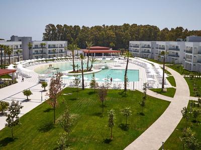 Moderner Hotelkomplex mit großem Pool und umliegenden Grünflächen unter klarem Himmel.