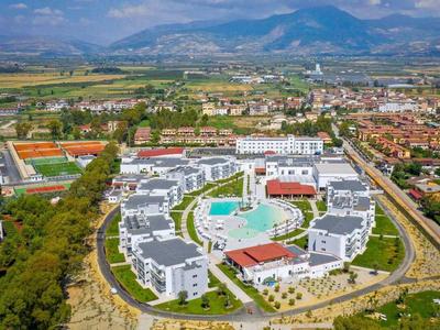 Vista aerea di un resort circolare con piscina in una città con montagne sullo sfondo.