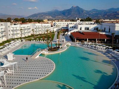 Large hotel pool with white lounge chairs and surrounding buildings under a clear sky with mountains.