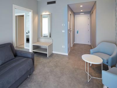 Bright hotel room with gray sofa, two blue armchairs, and small white table.