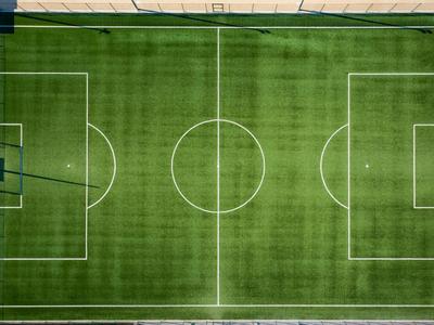 Green soccer field from above with clear white lines and goal areas.