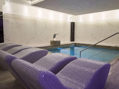 Piscina interna con lettini e illuminazione moderna in un'area spa rilassante.