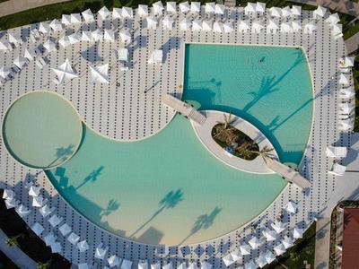 Vista aerea di una piscina moderna circondata da molti lettini bianchi e ombrelloni.