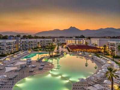Hotel di lusso con piscina illuminata e lettini al tramonto con sfondo montano.