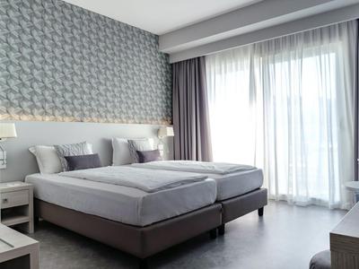 Modern hotel room with two single beds, gray decor, and large window with curtains.