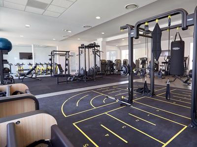 Moderner Fitnessraum mit Trainingsgeräten, Spiegeln und Sitzbereich in einem Hotel.