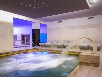 Area benessere moderna con vasca idromassaggio, getto d'acqua e zona salotto accogliente.