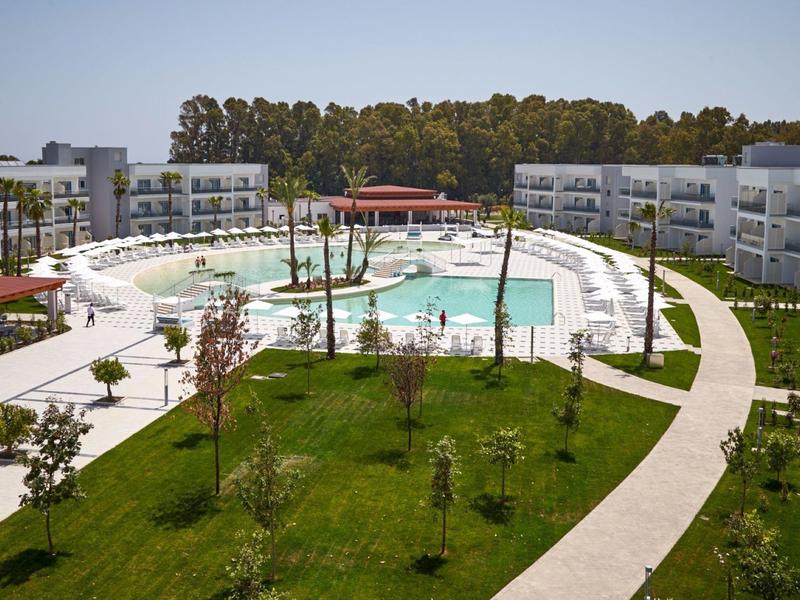 Complesso alberghiero moderno con grande piscina, sentieri circostanti e cortile verde.