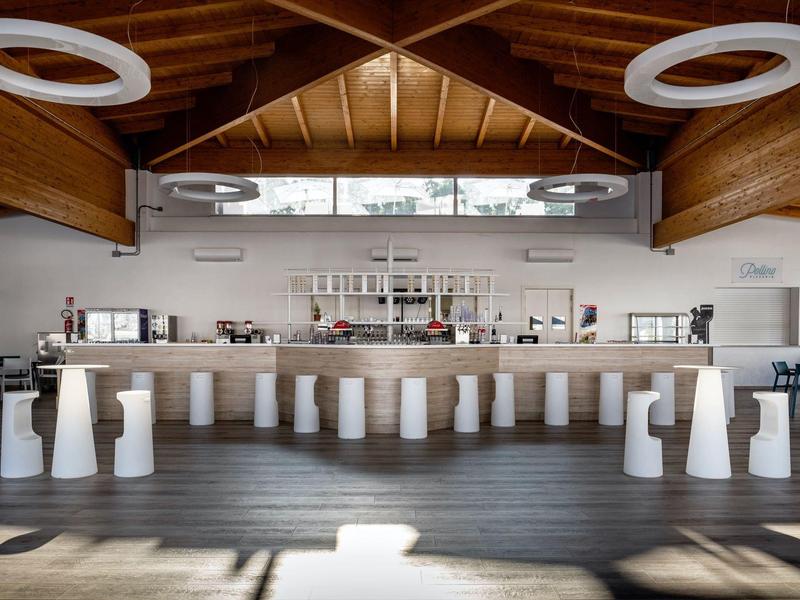 Area bar moderna in hotel con soffitto in legno, sgabelli bianchi eleganti e bancone illuminato.