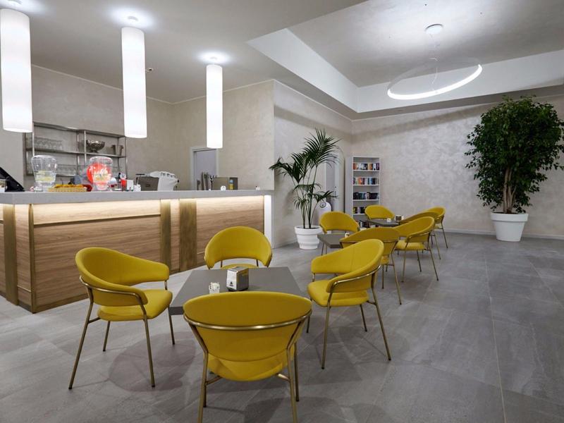 Area lounge moderna dell'hotel con sedie gialle e bancone in legno in un ambiente luminoso.
