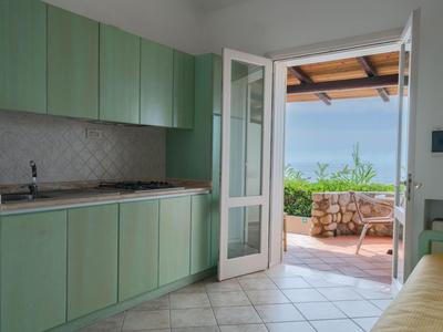 Küchenbereich mit grünen Schränken und geöffneter Tür zur Terrasse mit Blick auf das Meer.