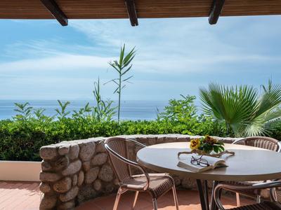 Terrasse mit Tisch, Stühlen und Blick auf das Meer und Pflanzen unter einem Holzvordach.