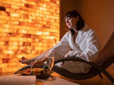 Frau in Bademantel entspannt sich auf Liegestuhl vor beleuchteter Salzsteinwand im Spa.