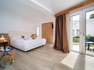 Jasna sypialnia z podwójnym łóżkiem, drewnianą podłogą, stolikami nocnymi i drzwiami na taras do ogrodu