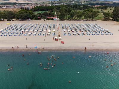 Plaża z parasolami, leżakami i ludźmi w wodzie przy czystym niebie.