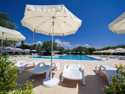 Espace de détente avec piscine, chaises longues et parasols sous un ciel bleu.