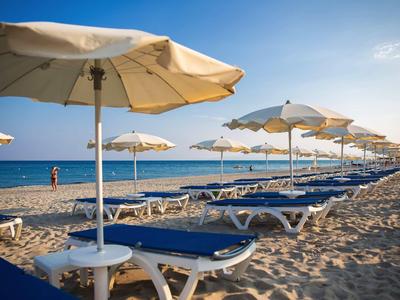 Rangée de chaises longues bleues sous parasols blancs sur plage de sable sous ciel clair