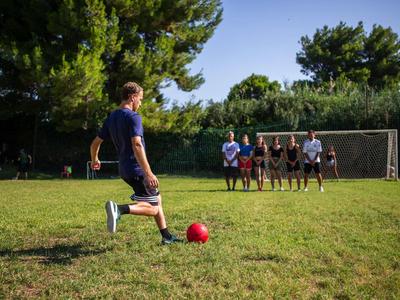 Personne tirant un ballon de football vers un mur de joueurs devant un but sur un terrain vert.