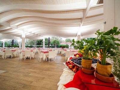 Zadaszony taras z białymi stolikami i krzesłami w hotelu, z roślinami i owocami na pierwszym planie.