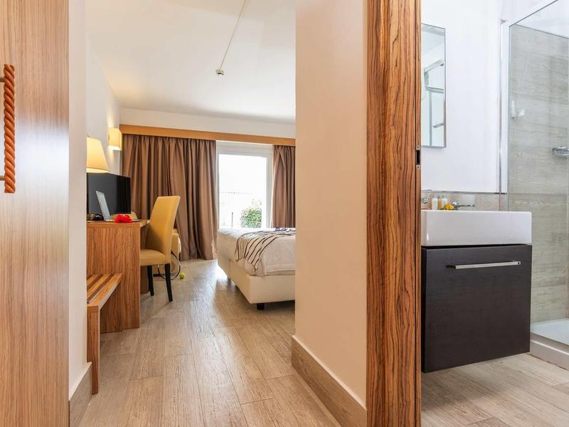 Widok na pokój hotelowy z łóżkiem, biurkiem i przyległą łazienką z prysznicem.