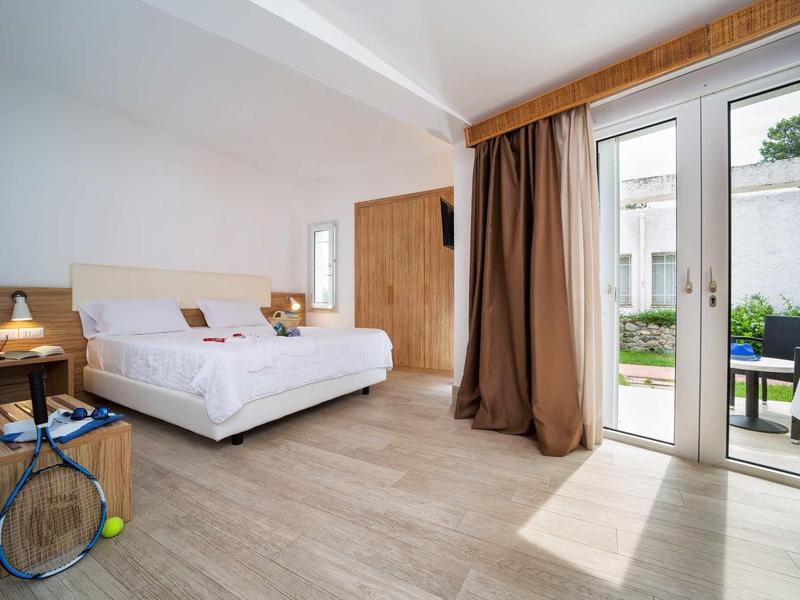 Jasna sypialnia z podwójnym łóżkiem, drewnianą podłogą, stolikami nocnymi i drzwiami na taras do ogrodu