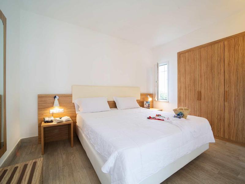 Jasna sypialnia z dużym łóżkiem, stolikami nocnymi i dużą drewnianą szafą.