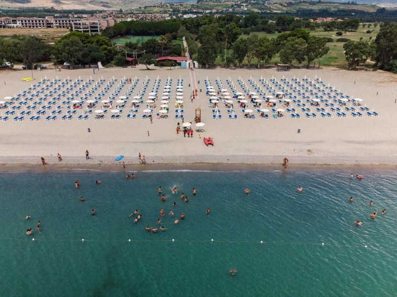 Plaża z parasolami, leżakami i ludźmi w wodzie przy czystym niebie.