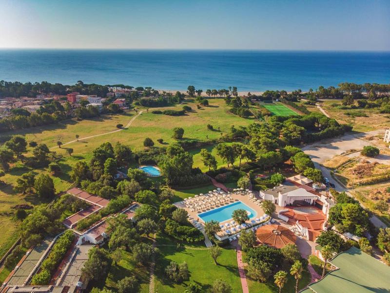 Widok z lotu ptaka na ośrodek z basenem obok terenów zielonych i widokiem na morze w tle.