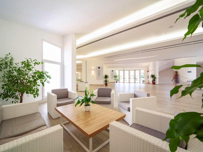 Jasna lobby hotelowa z białymi fotelami, drewnianym stołem i dużymi oknami