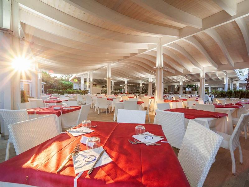 Jasno oświetlony ogródek restauracyjny z czerwonymi nakryciami stołów i białymi krzesłami.