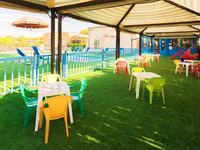 Colorful outdoor seating area with green lawn and covered tables beside a pool.
