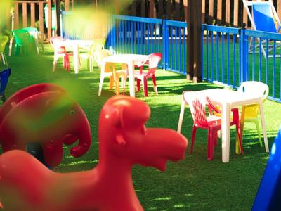 Colorful outdoor area with plastic tables, chairs, and play equipment on green artificial grass.