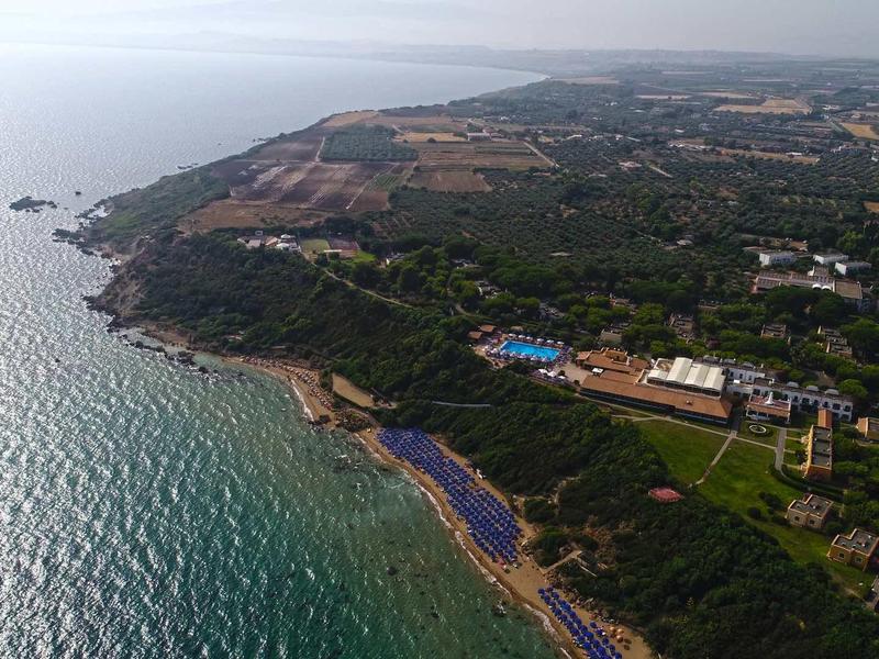 Aerial view of a coastline with beaches, green areas, and village houses by the sea.