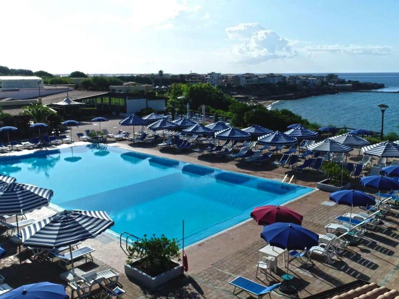 Large pool with sun loungers and umbrellas by the sea in a hotel resort.