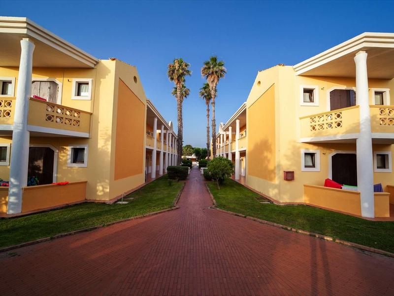 Two yellow holiday houses with columns and palm trees in the background under clear sky.