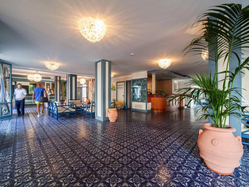 Hotel lobby with blue patterned tiles, large plants, and seating areas.