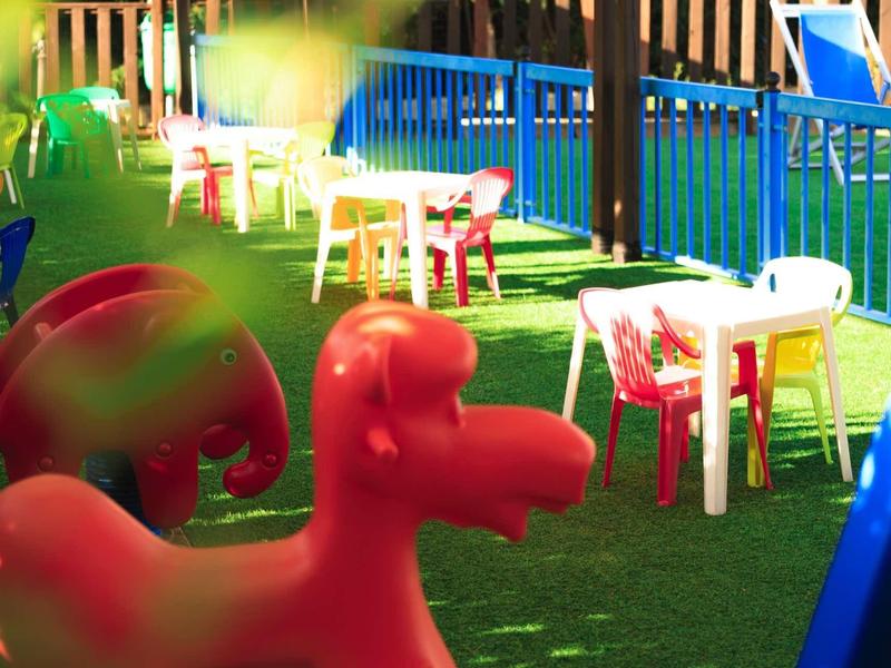 Colorful outdoor area with plastic tables, chairs, and play equipment on green artificial grass.