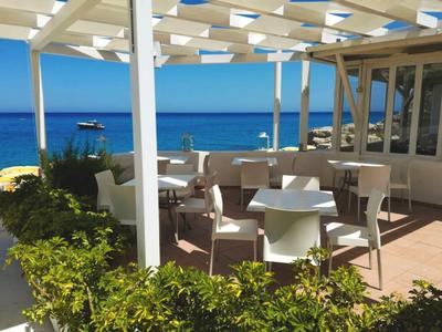 Terrasse d'hôtel avec tables et chaises blanches, vue sur la mer bleue sous un ciel clair.