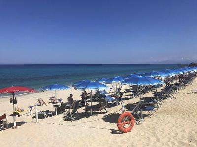 Sandstrand mit blauen Sonnenschirmen und Liegestühlen am Meer unter klarem Himmel.