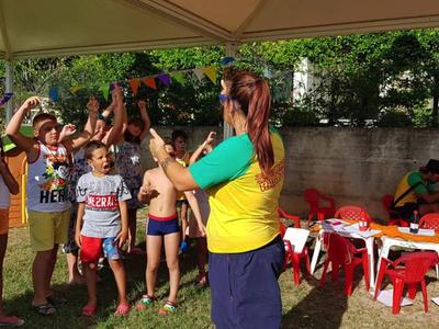 Děti si hrají venku s animátorem v žluto-modrém tričku vedle stolu s červenými židličkami