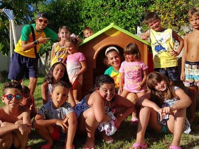 Skupina šťastných dětí hrajících si venku před malým domečkem na hraní na zahradě.