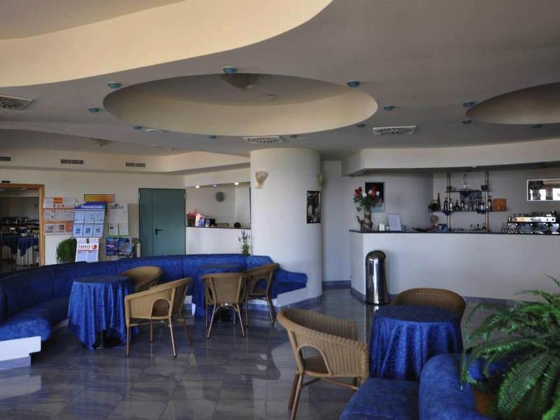 Světlý salonek s modkým posezením, stoly a moderním stropním osvětlením v hotelu.