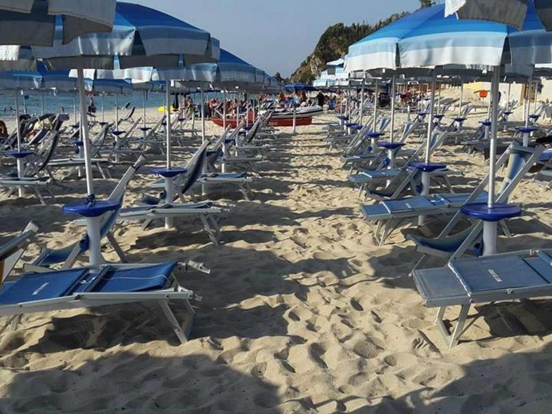 Řady modrých lehátek a slunečníků na písečné pláži pod jasnou oblohou.