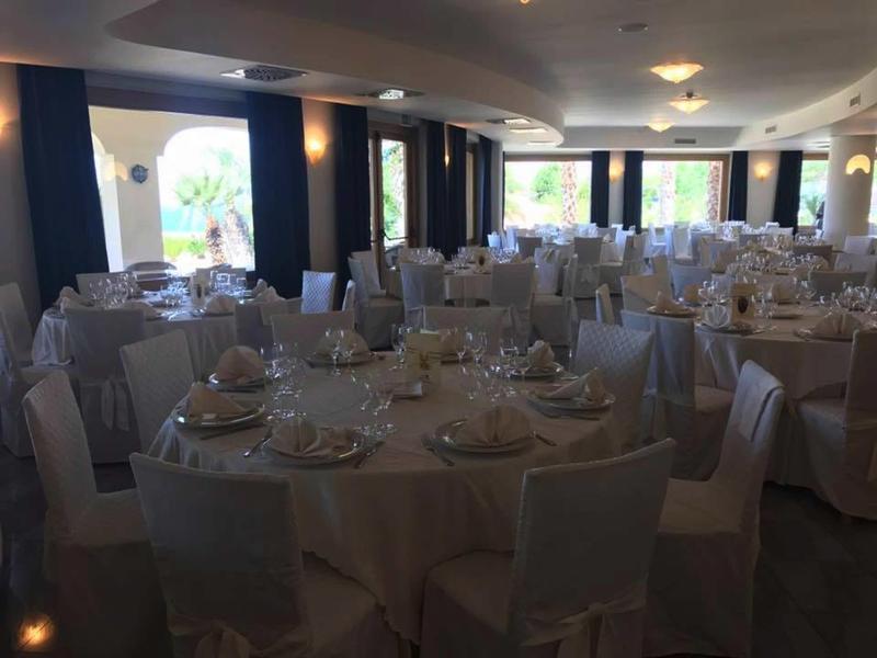 Sváteční banketní sál s kulatými prostřenými stoly a židlemi zakrytými bílým potahem.