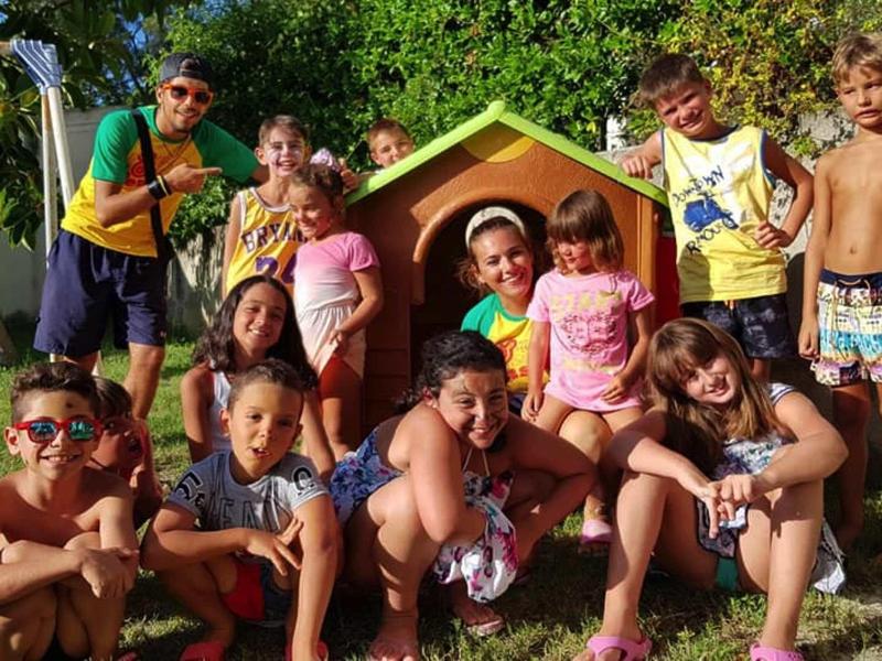 Skupina šťastných dětí hrajících si venku před malým domečkem na hraní na zahradě.