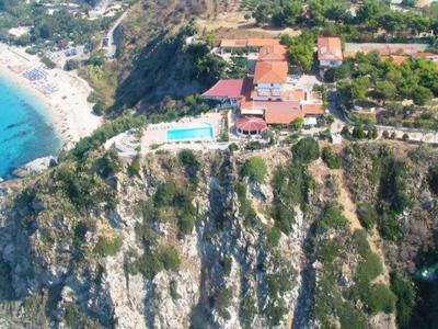 Vue aérienne d'un hôtel avec piscine sur une falaise surplombant la mer et une plage proche.