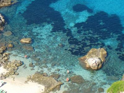 Eau turquoise claire avec rochers et plage de sable avec chaises longues.
