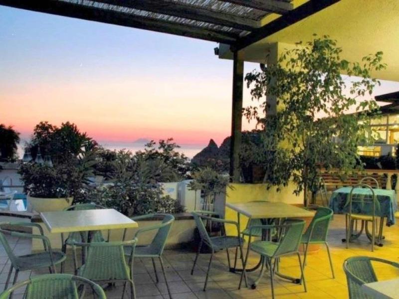 Terrasse extérieure avec chaises et tables au coucher du soleil avec des plantes et vue dégagée.