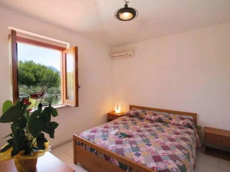 Chambre lumineuse avec fenêtre ouverte, lit double et plante en pot.